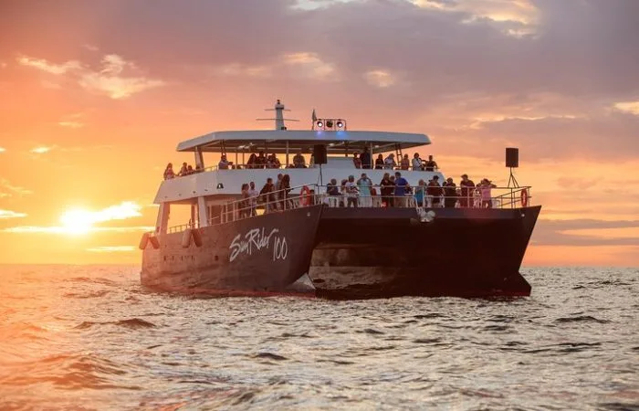 Catamaran rempli de personnes naviguant sur une mer au coucher du soleil