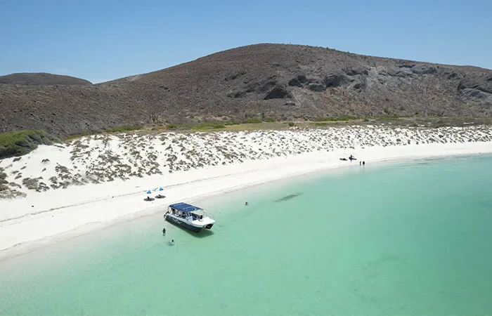 Plage de sable blanc, mer turquoise, bateau et quelques personnes