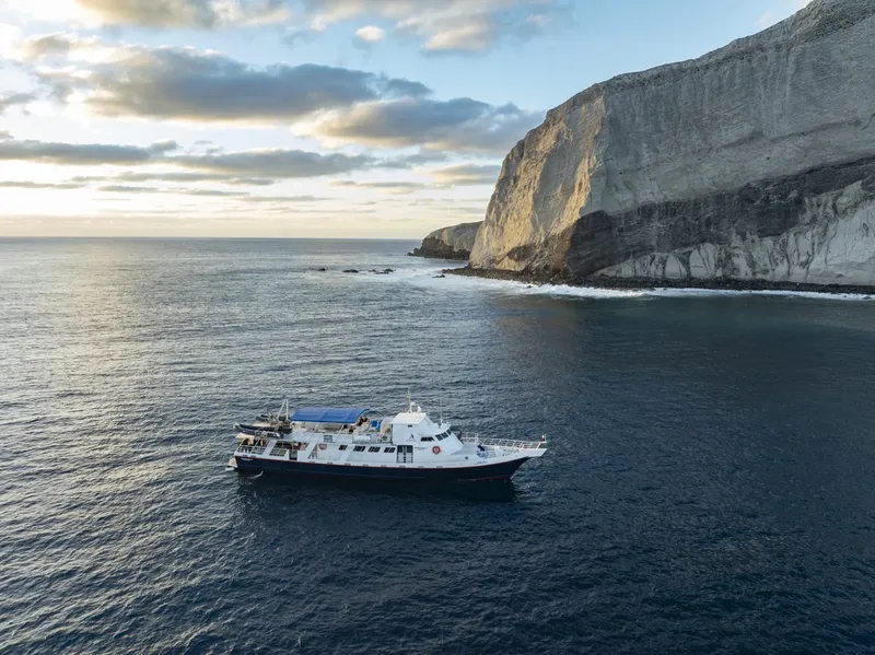 Bateau de plongée blanc naviguant en mer devant une falaise rocheuse