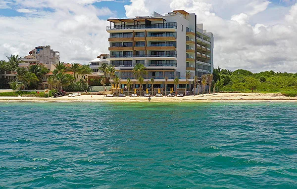 Bâtiment blanc avec balcons, plage de sable et mer turquoise