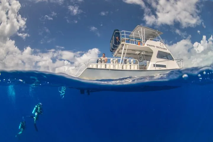 Bateau de plongée avec des plongeurs en dessous, ciel bleu nuageux