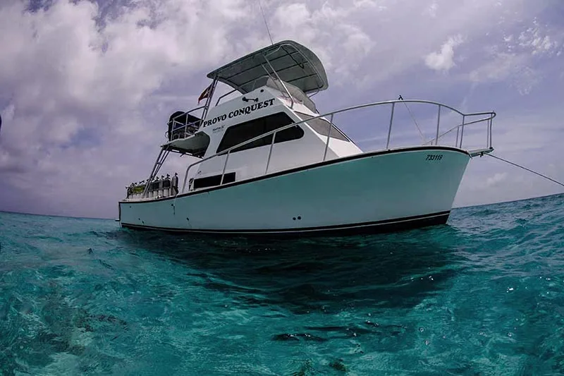 Bateau de plongée turquoise avec des passagers, ciel nuageux et eau claire