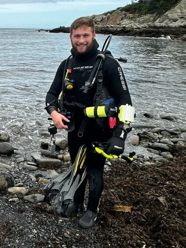 Plongeur souriant en combinaison complète sur une plage rocheuse