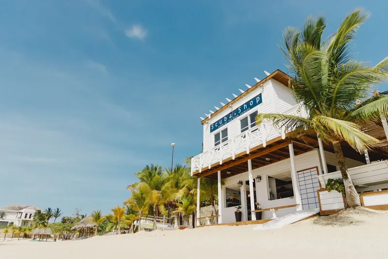 Bâtiment blanc avec enseigne Scuba Shop sur une plage ensoleillée