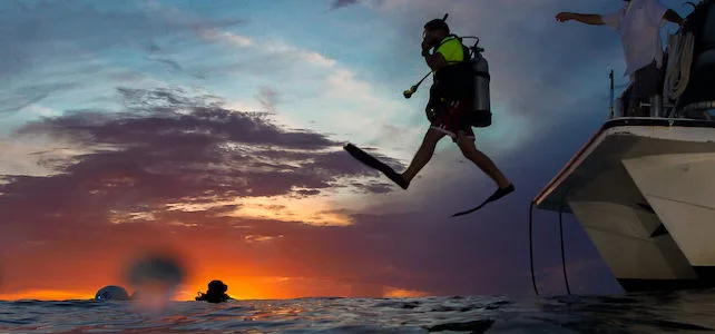 Plongeur s'élance d'un bateau au coucher du soleil en mer