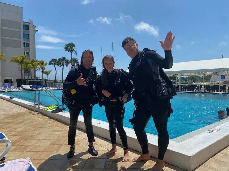 Trois plongeurs souriants en combinaison près d'une piscine ensoleillée