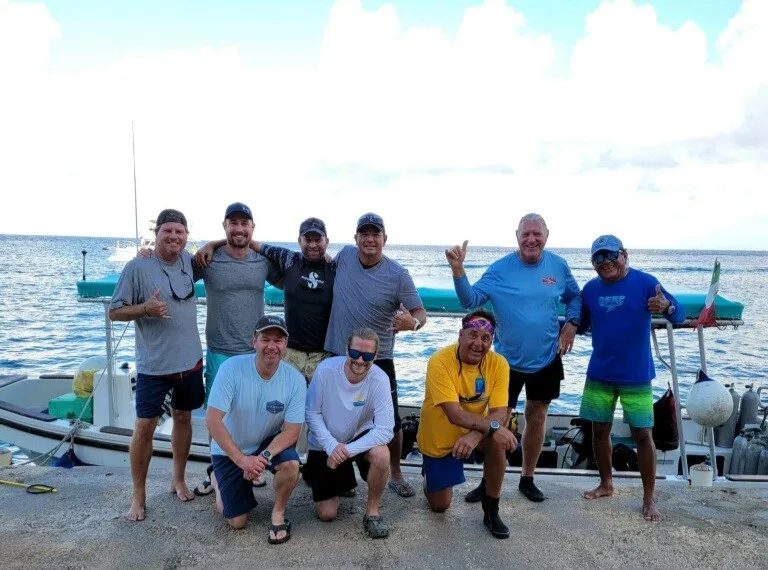 Groupe de plongeurs souriants posant devant un bateau sur un quai