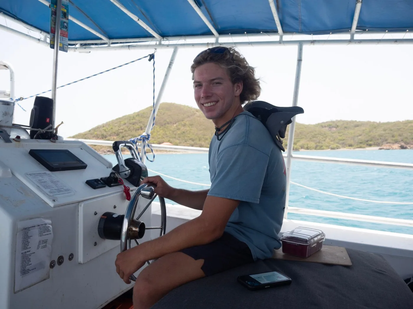 Jeune homme souriant tient la barre d'un bateau en mer