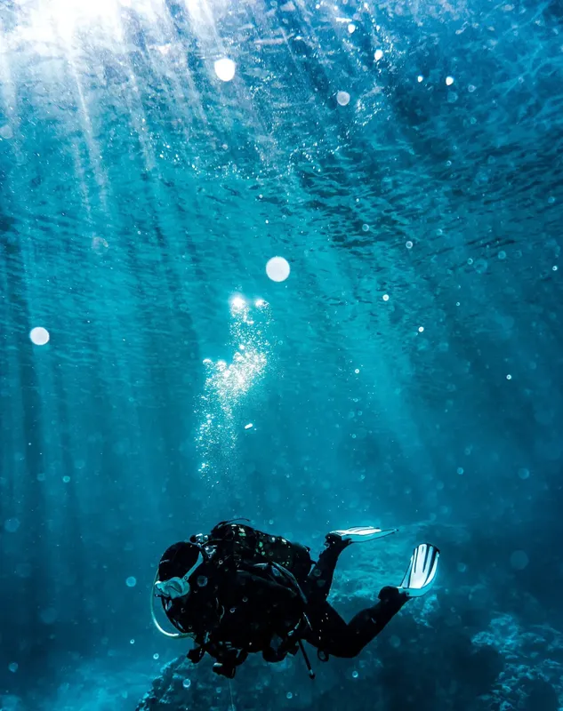 Plongeur en combinaison noire explore les profondeurs bleues sous la surface