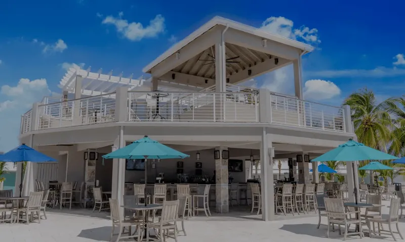 Terrasse d'un bâtiment avec bar, tables et parasols, ciel bleu
