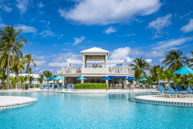 Piscine turquoise avec transats, palmiers et bâtiment blanc sous ciel bleu