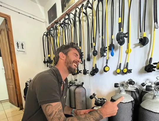 Un homme souriant montre un équipement de plongée dans un local