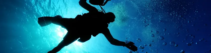 Plongeur en silhouette remontant vers la surface dans l'eau bleue
