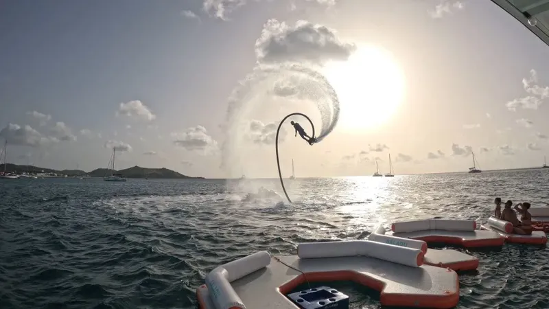 Personne pratiquant le flyboard au-dessus de l'eau, bateaux et ciel nuageux