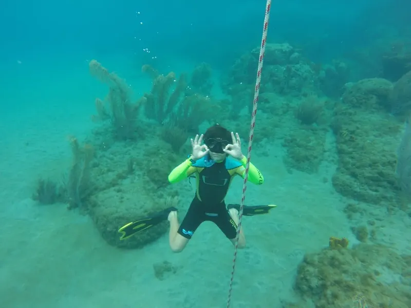Plongeuse faisant un signe OK sous l'eau avec coraux et sable