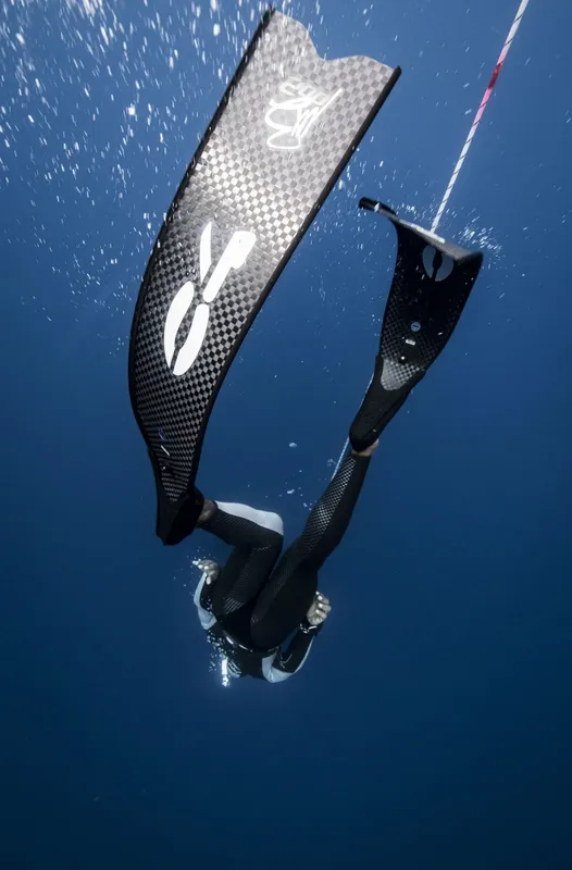 Apnéiste en combinaison noire descendant avec ses palmes dans l'eau bleue