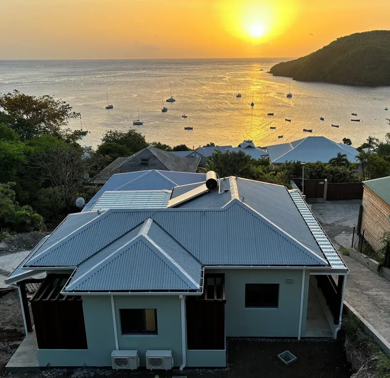 Bâtiment turquoise avec toits métalliques, bateaux amarrés au loin, coucher de soleil
