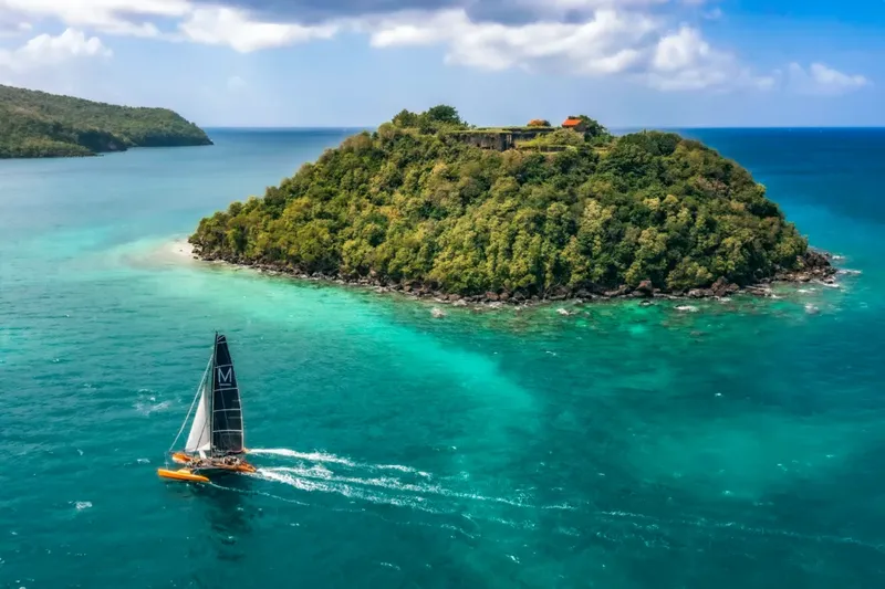 Catamaran naviguant en mer turquoise devant une île verdoyante