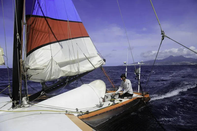 Homme naviguant sur un catamaran en mer avec une voile colorée