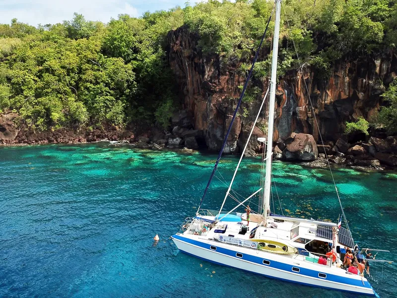 Catamaran bleu amarré dans une eau turquoise près d'une côte rocheuse
