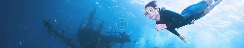 Plongeuse en apnée nageant au-dessus d'une épave sous-marine éclairée