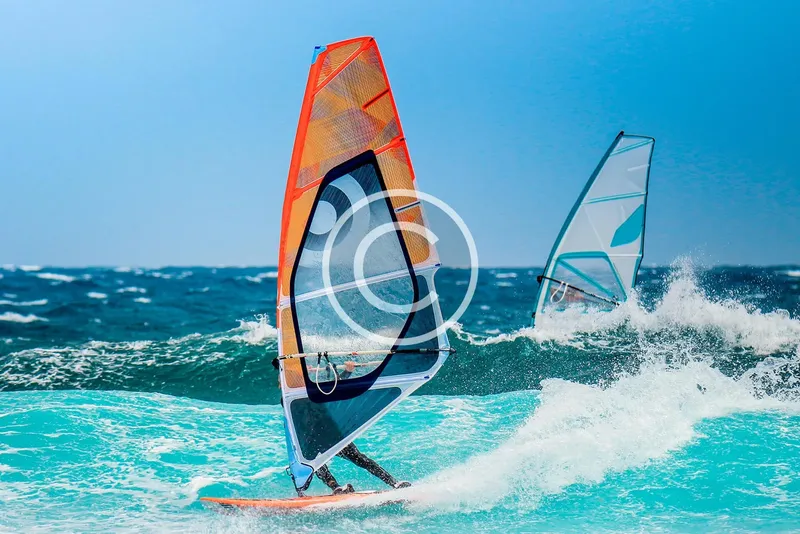 Deux windsurfeurs naviguent sur une mer agitée sous un ciel bleu