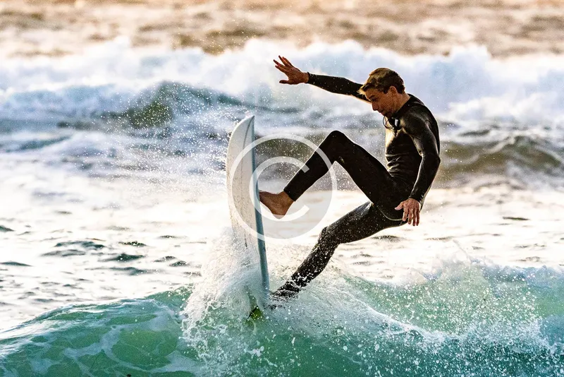 Surfeur en pleine action sur une vague, combinaison noire, ciel clair