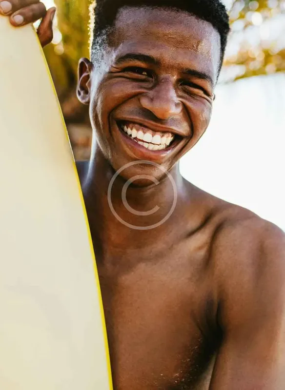 Jeune homme souriant tenant une planche de surf, regardant la caméra
