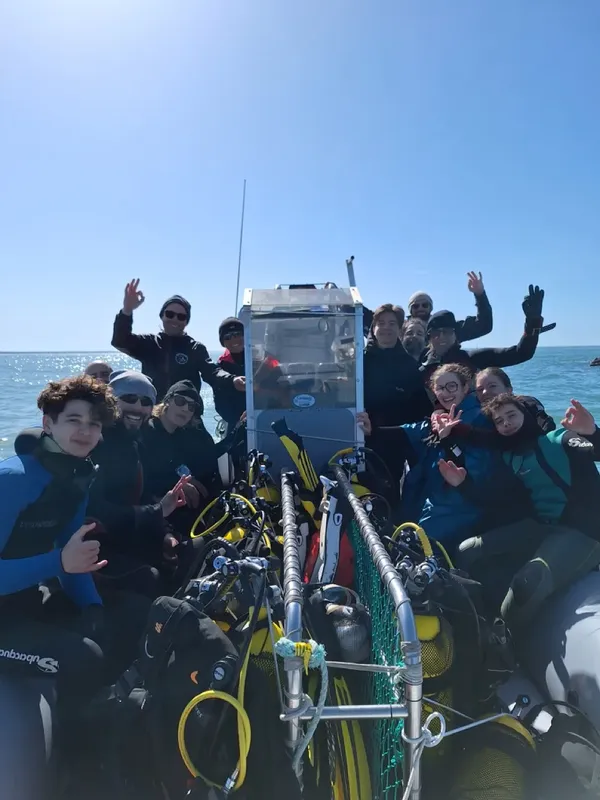 Groupe de plongeurs souriants sur un bateau en mer, équipement visible