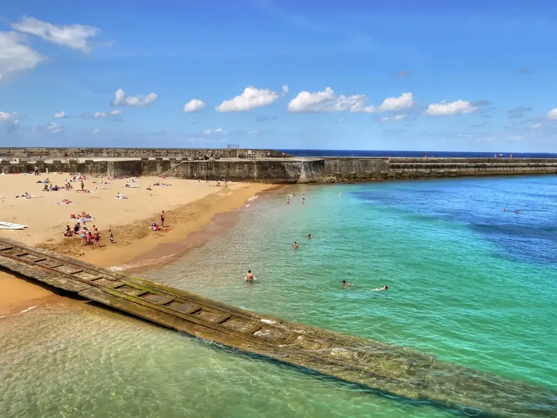Plage ensoleillée avec des baigneurs et une digue rocheuse turquoise