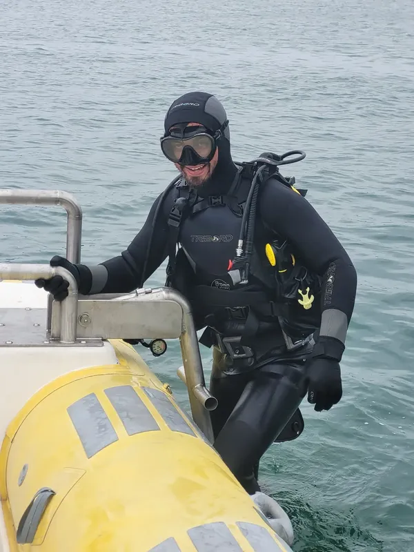 Plongeur en combinaison noire sort d'un bateau jaune en mer