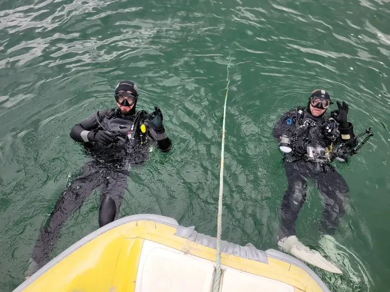 Deux plongeurs en combinaison flottent près d'une embarcation jaune