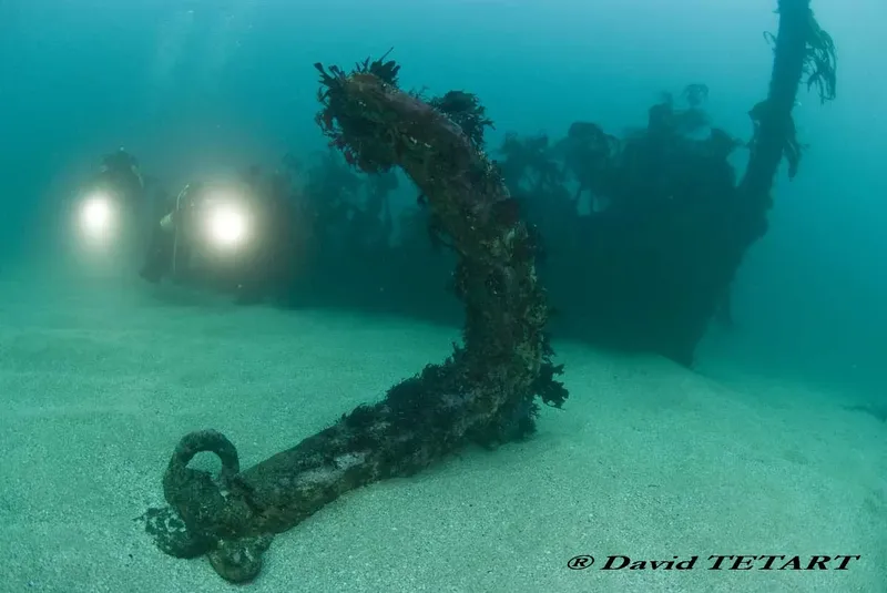 Epave rouillée sous l'eau avec des lumières de plongeurs visibles
