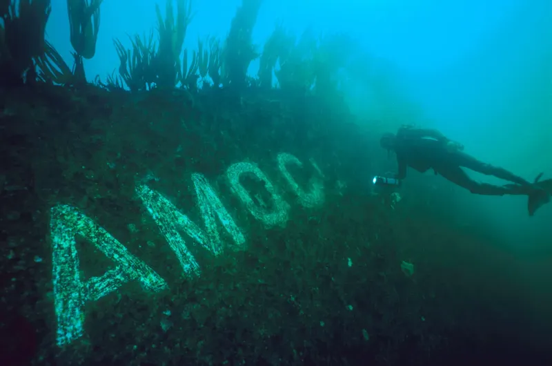 Plongeur explorant une épave avec des lettres visibles sous-marine