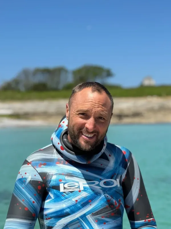 Homme souriant en combinaison de plongée devant un paysage marin