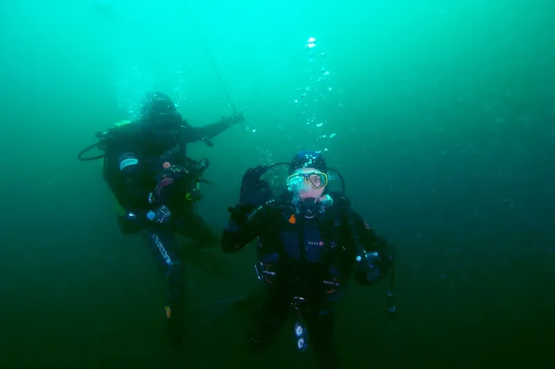 Deux plongeurs en combinaison scrutent les profondeurs sous-marines, bulles