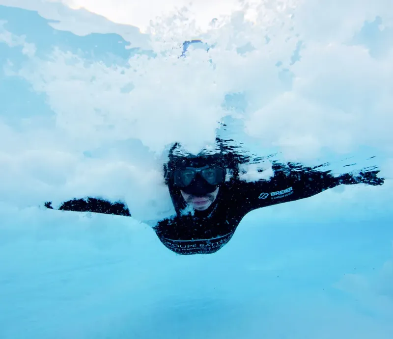 Plongeur en combinaison noire nageant sous une surface glacée claire