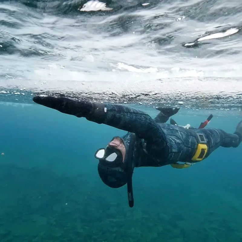 Apnéiste en combinaison nageant sous la surface de l'eau bleue