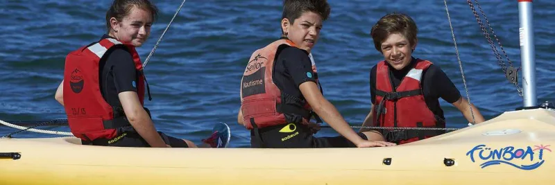 Trois jeunes souriants en gilets de sauvetage sur un bateau jaune
