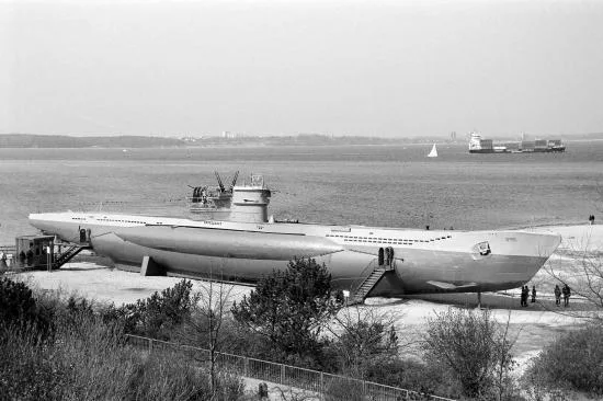 Sous-marin échoué sur une berge, quelques personnes se promènent autour