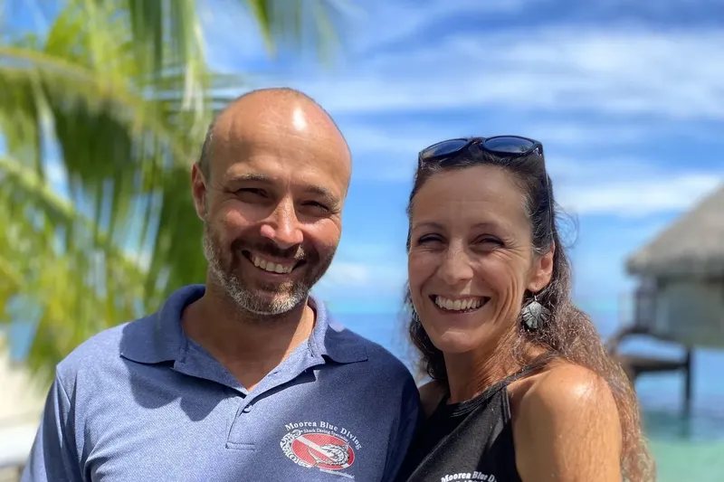 Deux personnes souriantes posent en extérieur, ciel bleu et végétation