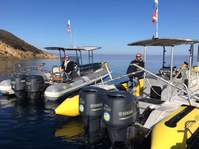 Deux hommes sur des bateaux semi-rigides amarrés dans une crique ensoleillée