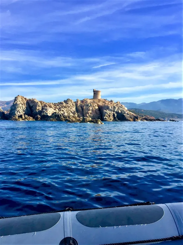 Vue d'une île rocheuse avec une tour, mer bleue et ciel clair