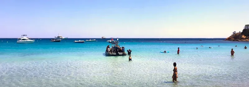 Plage ensoleillée avec des baigneurs et plusieurs bateaux amarrés au large
