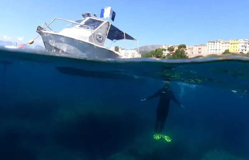Plongeur en combinaison noire nageant sous un bateau de plaisance bleu