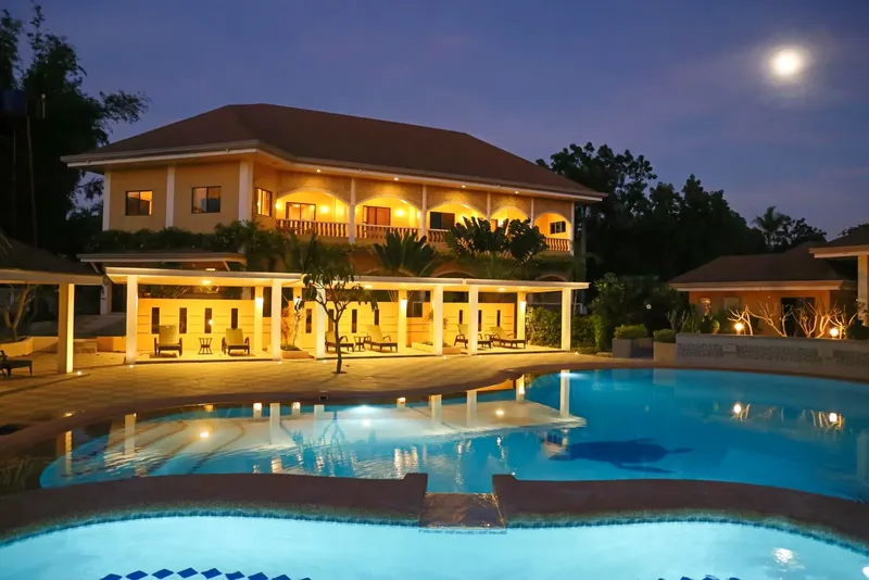 Bâtiment éclairé la nuit avec piscine et végétation luxuriante