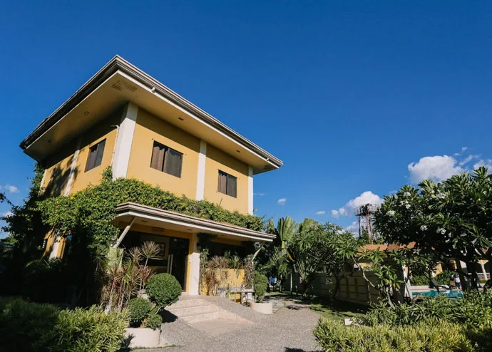 Bâtiment jaune à deux étages avec végétation luxuriante et ciel bleu