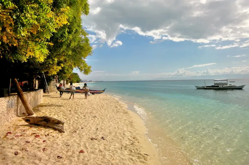 Plage de sable blanc avec des personnes et un bateau en mer