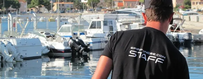 Homme dos à la caméra, port avec bateaux et texte sur t-shirt