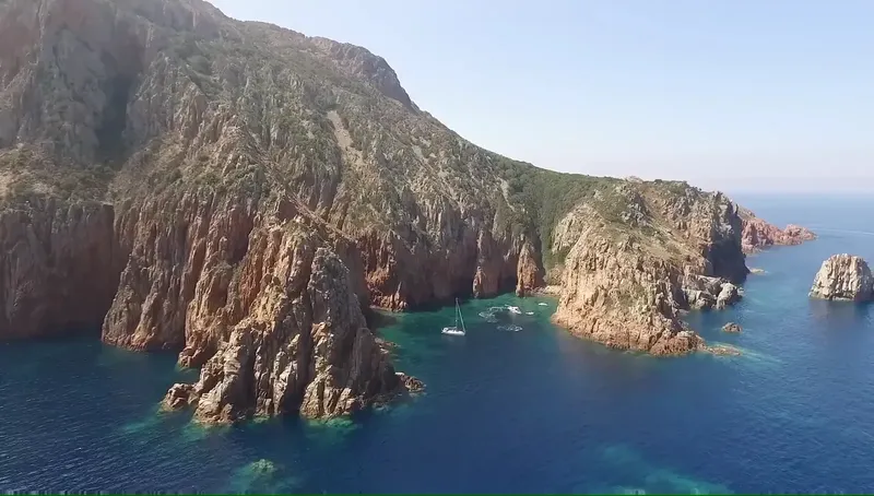 Côte rocheuse avec des bateaux à voile dans une eau turquoise claire